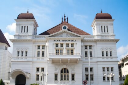 Front facade of Bank Indonesia building, a white neoclassical structure with red-tiled roof and decorative detailing under a blue sky