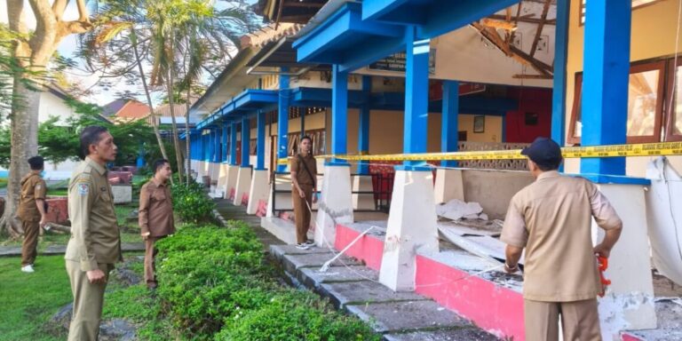 Gedung-SMA-1140x570 - Mabur.co Officials in tan uniforms stand outside a blue-painted building under renovation, yellow caution tape blocking the entrance, debris nearby.