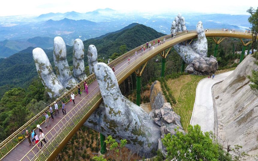 Pedestrian walkway held by giant stone hands, curving over a valley with travelers along a golden bridge.