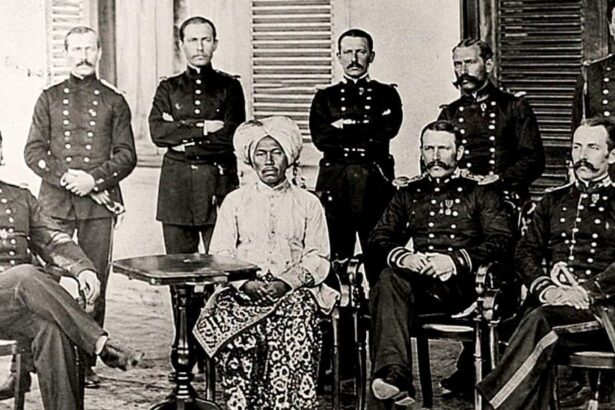 Group of uniformed military officers surrounding a central seated African woman in a turban and patterned dress; a colonial-era portrait.