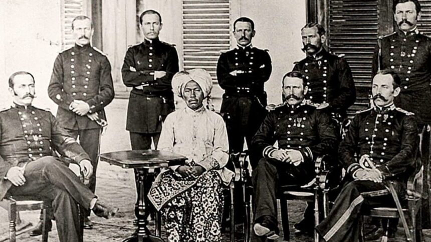 Group of uniformed military officers surrounding a central seated African woman in a turban and patterned dress; a colonial-era portrait.