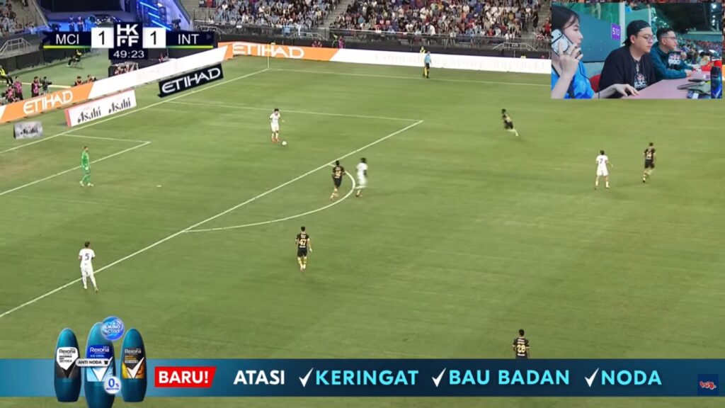 Soccer match in progress; scoreboard shows 1-1 at 49:23, players on a green pitch with Etihad ads along the sideline; inset live-cabinet of commentators in top-right.