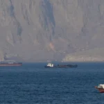 Calm sea with several ships and a rocky coastline in the distance.