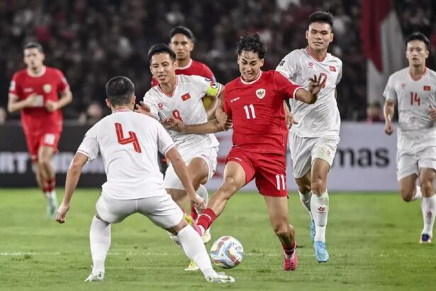 Soccer match in progress: a player in red (number 11) kicks the ball while white-jersey opponents converge.