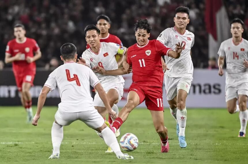 Soccer match in progress: a player in red (number 11) kicks the ball while white-jersey opponents converge.