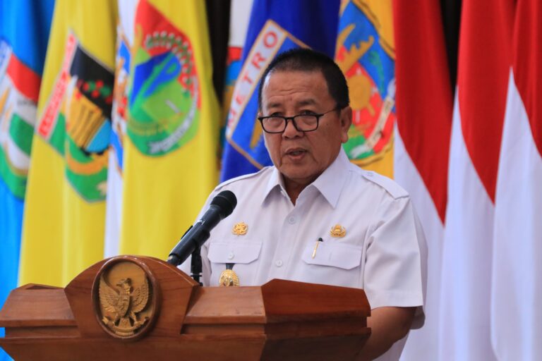 Official in white uniform giving a speech at a podium with a microphone, flags in the background.