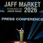 Speaker at a podium on a lit stage during a press conference with a large banner reading 'JAFF MARKET 2026' and 'POWERED BY AMAR BANK' in the background.
