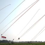 Outdoor festival with dozens of long strings of decorative kites or banners across a clear sky; Indonesian flag visible in foreground.