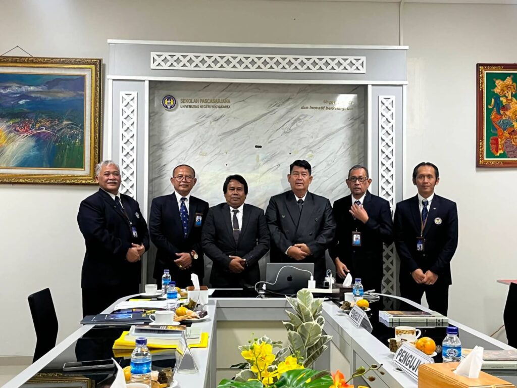 Six men in dark suits pose behind a conference table in a formal meeting room. Laptops, water bottles and paperwork are on the table, marble backdrop behind them, university logo visible on the wall and framed art on both sides.