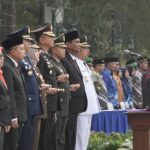 Line of uniformed officials and civilians standing at a formal ceremony behind a podium and microphones.