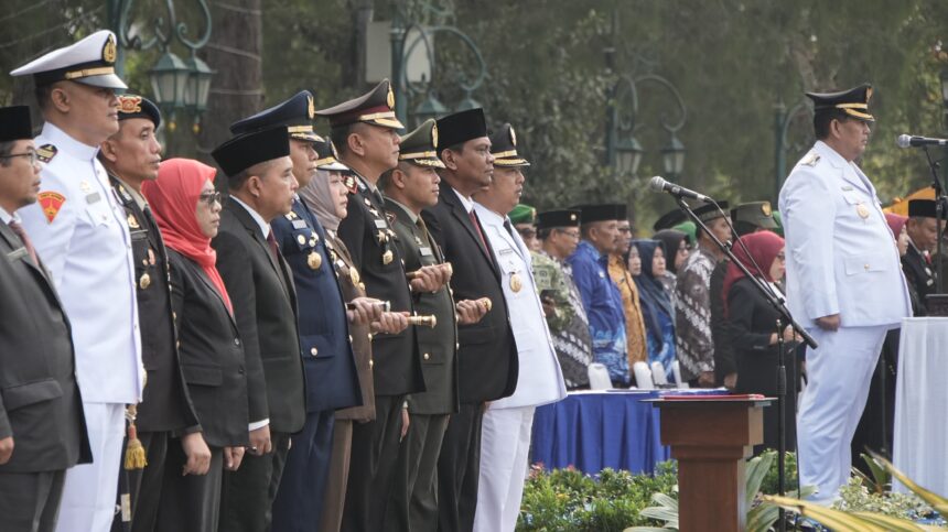 Line of uniformed officials and civilians standing at a formal ceremony behind a podium and microphones.