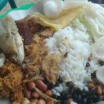 Plate with white rice, fried chicken, peanuts, fried onions, beans, and prawn crackers; a traditional mixed Malaysian nasi lemak style dish.