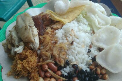 Plate with white rice, fried chicken, peanuts, fried onions, beans, and prawn crackers; a traditional mixed Malaysian nasi lemak style dish.