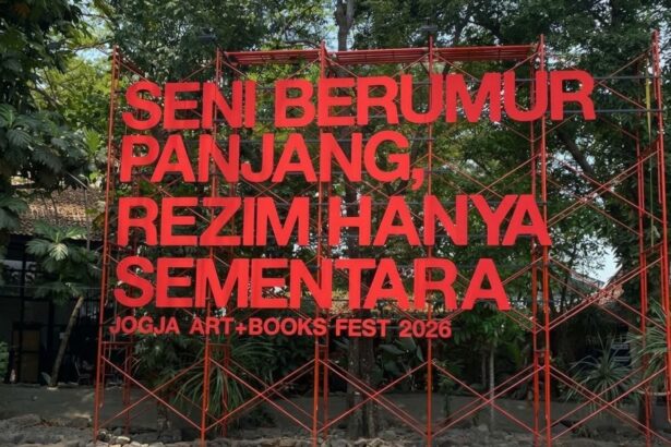 Large red metal sculpture with Indonesian text announcing Jogja Art + Books Fest 2026, set among trees outside.
