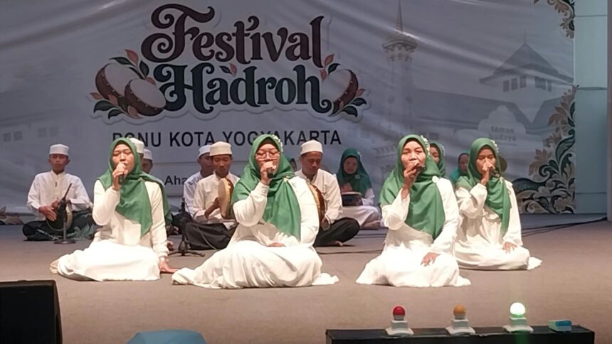Group of young performers in white robes and green headscarves singing on a stage at a Festival Hadroh event in Yogyakarta, with musicians in the background.