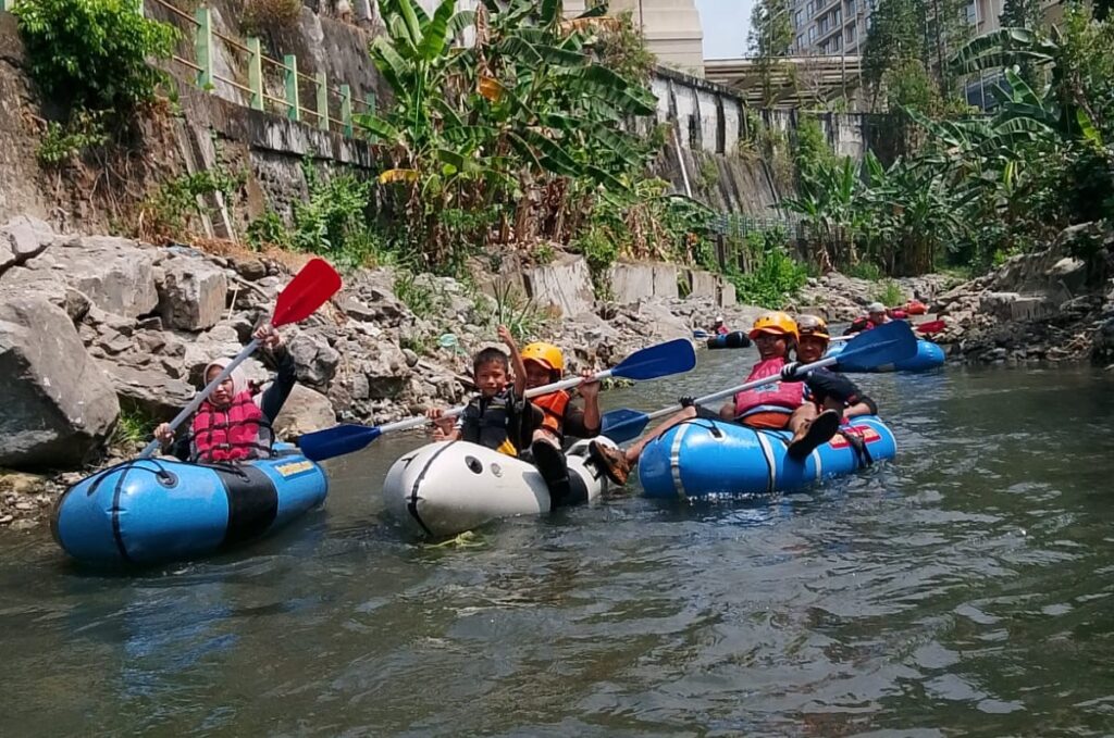 Group of people in inflatable tubes and life jackets paddling down a rocky, leafy river canyon.