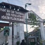 Signboard for Pusat Seni Tari Tradisional Gaya Yogyakarta in front of a white building and archway (Indonesia). Use prompts: traditional dance center sign.