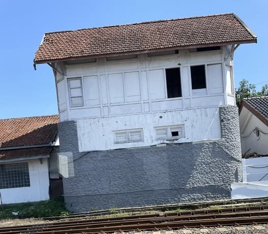 Old white two-story building with a red-tiled roof beside railway tracks, resting on a gray stone foundation.