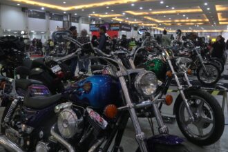 Indoor motorcycle show with a glossy blue cruiser in the foreground, chrome parts and round headlight, others lined up in the background.