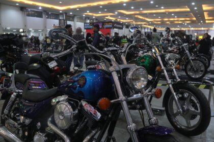Indoor motorcycle show with a glossy blue cruiser in the foreground, chrome parts and round headlight, others lined up in the background.