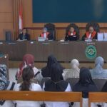 Courtroom scene with five judges in red robes seated at the bench, Indonesian flag behind them, audience watching.