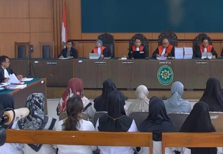 Courtroom scene with five judges in red robes seated at the bench, Indonesian flag behind them, audience watching.
