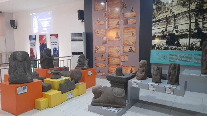 Display of various stone statues and carvings arranged on orange and yellow pedestals in a museum gallery, with informational plaques nearby.