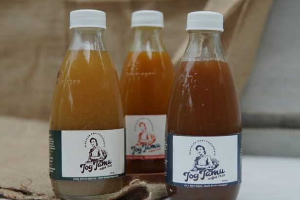 Three glass bottles with white caps containing brown liquid sit on a wooden surface; front labels show a person and the word 'Jog Jam'.