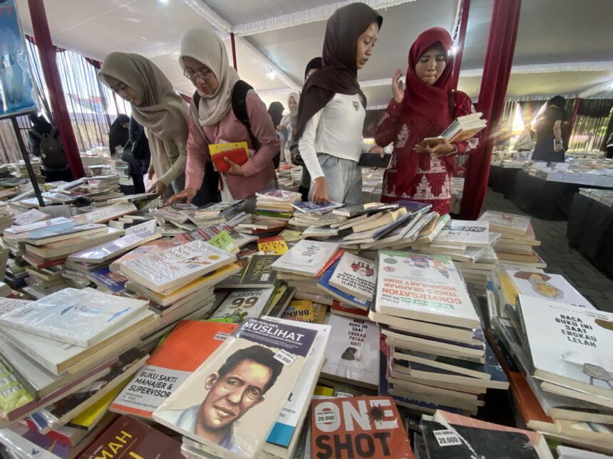 IMG_0042 - Mabur.co Women in hijabs browse a crowded book stall with tables piled with books inside a tent-like market area.