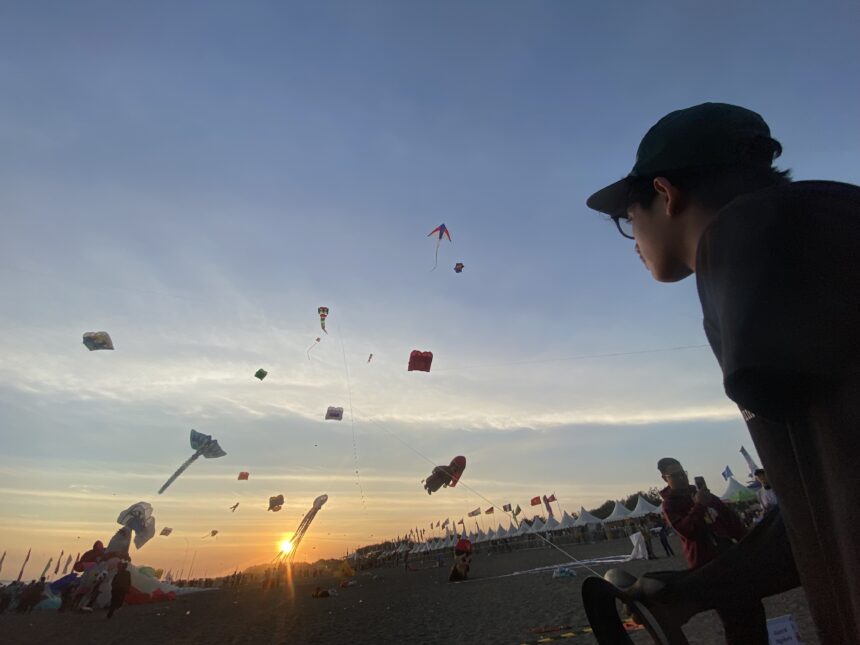 Kite festival at sunset with numerous colorful kites in the sky and people gathered along the beach.