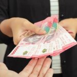 Two hands exchanging a fan of pink banknotes, cash transfer between people.