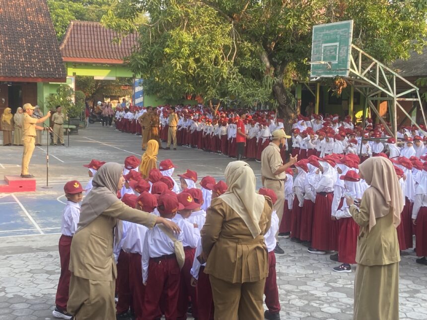 IMG_0278 - Mabur.co Large group of schoolchildren in white shirts, red caps and maroon skirts/pants standing in rows for an outdoor assembly, supervised by teachers in tan uniforms.