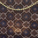Pale yellow braided cord laid diagonally on a dark blue and brown patterned fabric to show contrast against the textile pattern.
