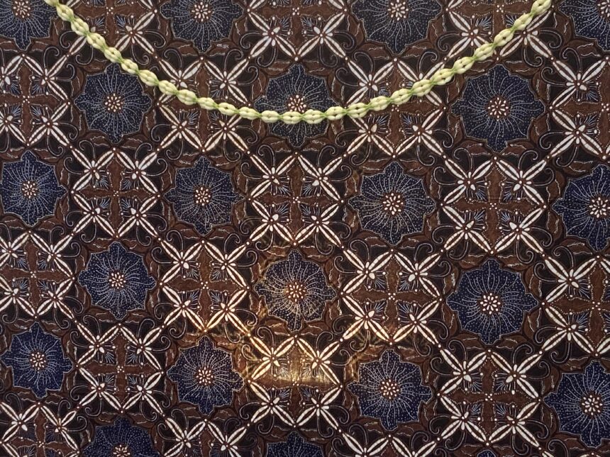 Pale yellow braided cord laid diagonally on a dark blue and brown patterned fabric to show contrast against the textile pattern.