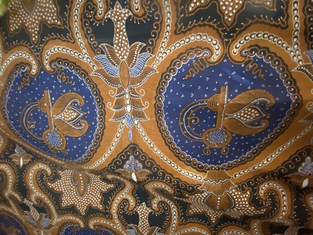 Decorative batik fabric with swirling orange and blue floral motifs and white dot accents.