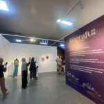 Group of visitors at an exhibition hall, some taking photos, beside a purple wall advertising Inacraft Festival 2026.