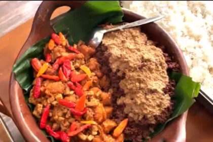 Clay pot with white rice on the side, containing a colorful stir-fry of minced meat and red/yellow peppers on the left and a crumbled topping on the right.