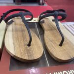 Two brown wooden flip-flops with black textured straps on a store display shelf