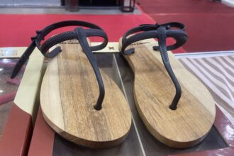 Two brown wooden flip-flops with black textured straps on a store display shelf