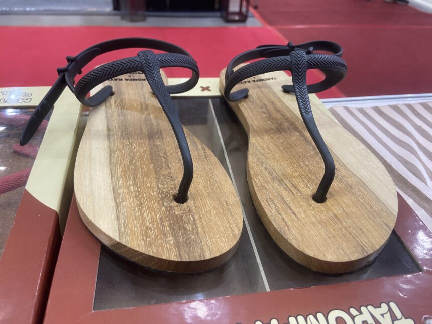 Two brown wooden flip-flops with black textured straps on a store display shelf