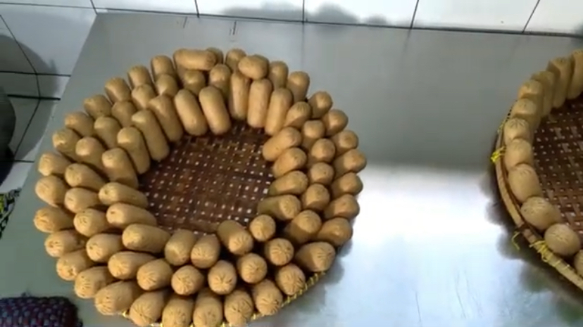 Ring of small bread rolls arranged in a circle on a perforated baking tray in a bakery setting.