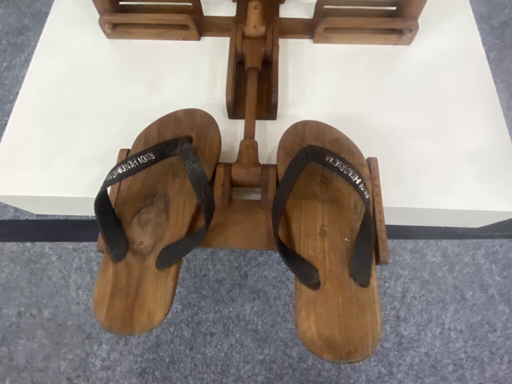 IMG_0461 - Mabur.co Top-down view of two wooden sandals with black straps, seen from above on a light floor.