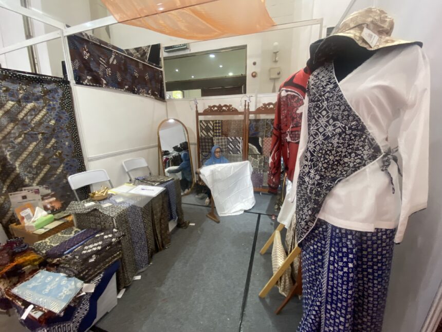 Fabric booth with patterned textiles on tables and racks; mannequin in a blue-and-white patterned dress on the right.