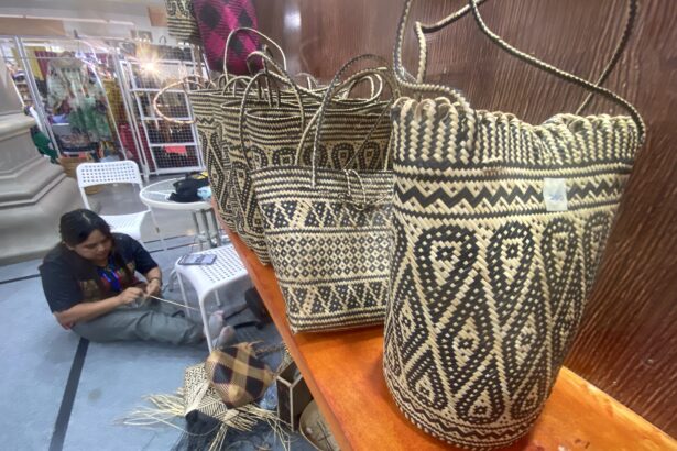 Rows of black-and-natural woven baskets on a wooden display, with a person weaving in the background at a market stall