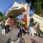Public gate with arch reading 'Yogyakarta' and workers sweeping the sidewalk outside the entrance.