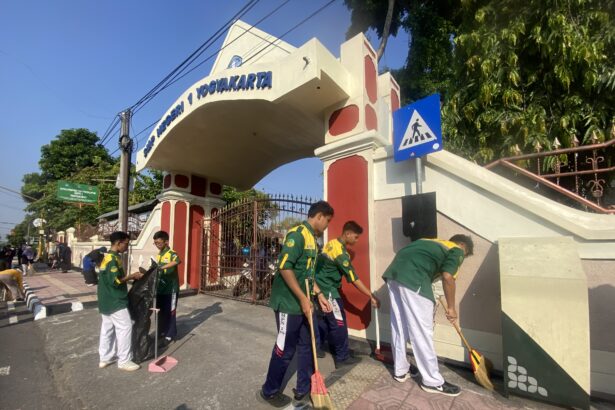 Public gate with arch reading 'Yogyakarta' and workers sweeping the sidewalk outside the entrance.
