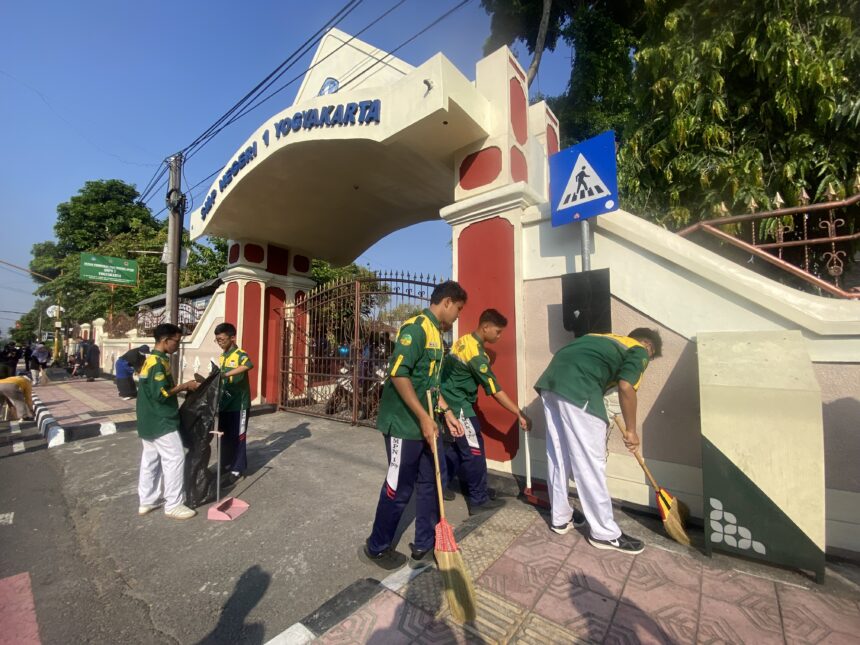 Public gate with arch reading 'Yogyakarta' and workers sweeping the sidewalk outside the entrance.