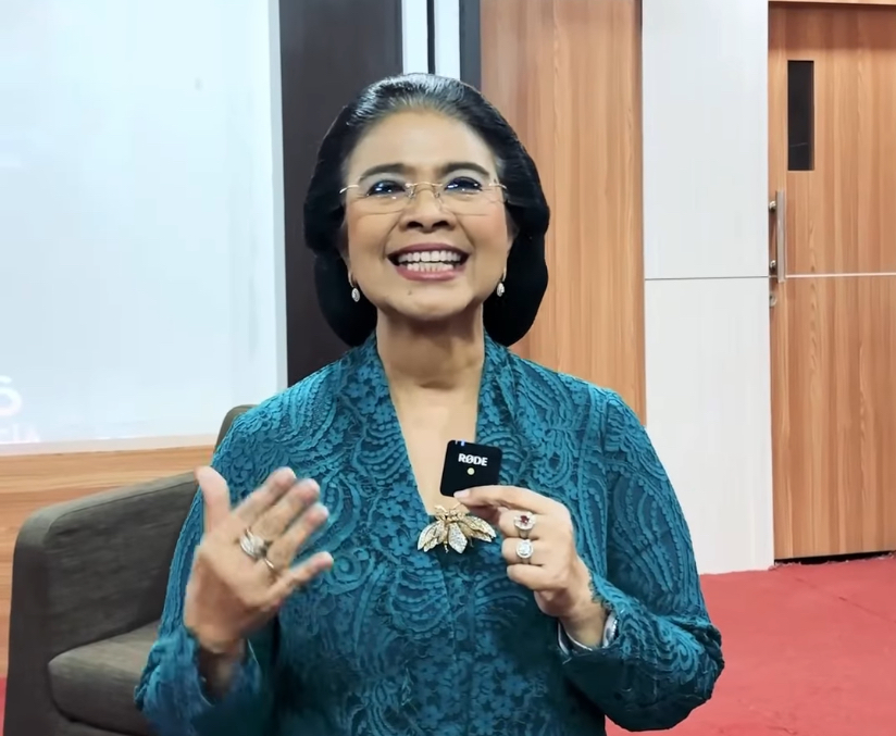 Smiling woman in a teal patterned blouse holds a small RODE microphone during a talk.
