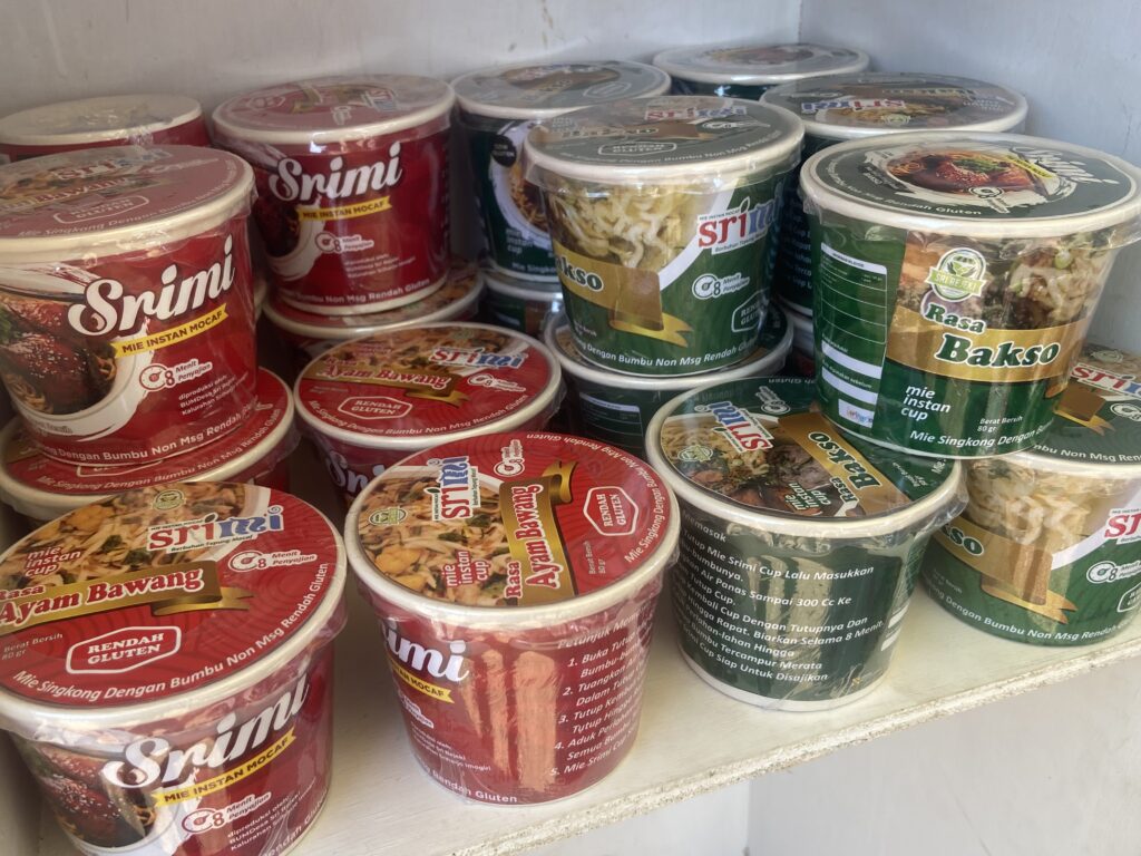 IMG_0909 - Mabur.co Assorted instant noodle cups arranged on a store shelf with colorful red, green, and yellow packaging.
