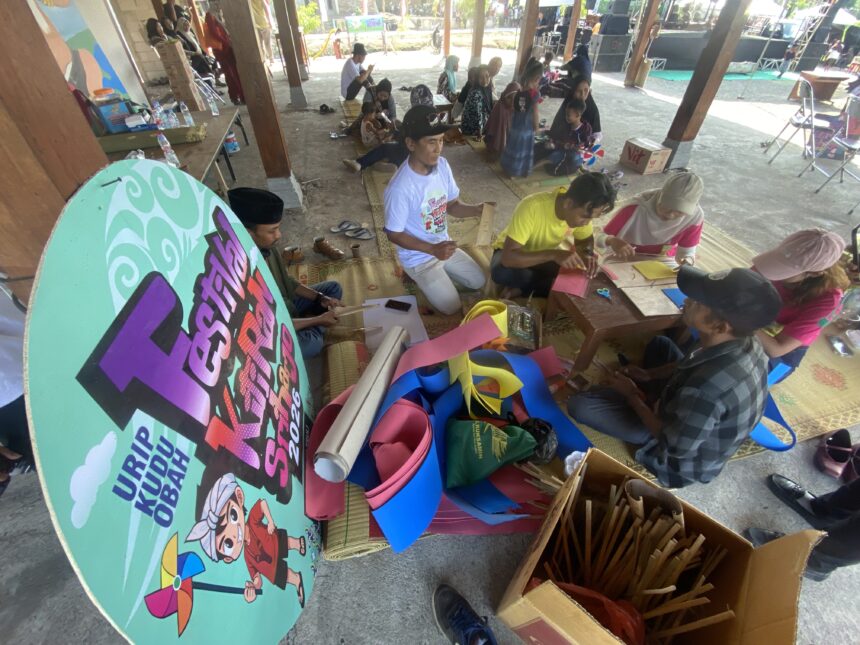 Group of people making paper crafts on mats under a pavilion at a daytime outdoor workshop.